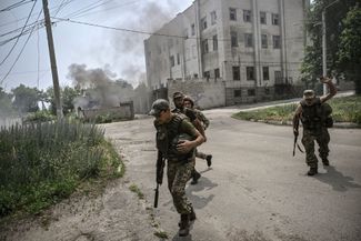 Украинские военные бегут в укрытие во время российского артиллерийского обстрела в городе