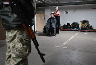 Женщина стрижет военнослужащего территориальных сил обороны на подземной парковке в Киеве