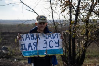 Мальчик с табличкой, на которой написано «Кофе, чай для ВСУ», у дороги недалеко от села Дубовое