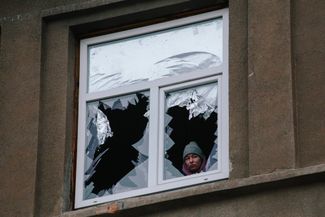Женщина смотрит из разбитого взрывом окна в Харькове
