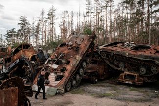 Офицер украинской полиции идет мимо уничтоженных боевых машин армии РФ, свезенных на комбикормовый завод