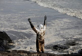 Рабочий подает сигналы коллегам, очищающим от нефти побережье города Лима. 19 января 2022 года