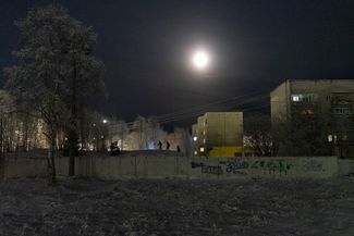 A view of the city of Murmansk at night. In the distance, three children play in the snow. The buildings are typical of the Soviet era.