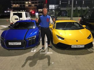 Andrey Plotnitsky (a.k.a. Kovalsky) standing between two Evil Corp sportscars.
