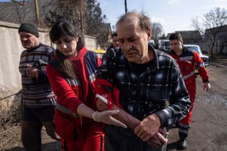 Медработник помогает раненному в результате российского обстрела мужчине дойти до машины скорой помощи