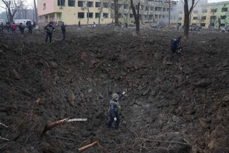 Украинские военные и спасатели рядом с воронкой от снаряда, упавшего во дворе мариупольского роддома. 9 марта 2022 года