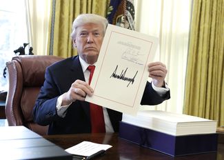 Дональд Трамп показывает подписанный законопроект о налоговой реформе. 22 декабря 2017 года
