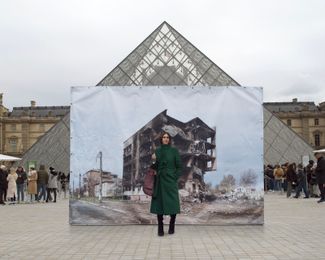 Twenty-five-year-old model Viktoriia stands in front of a photograph showing another destroyed apartment building in Borodyanka. Captured by photojournalist Yuliа Ovsyannikova, the image was displayed by the Louvre Pyramid in Paris, France.