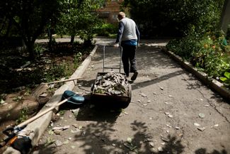 Мужчина тянет за собой тележку с обломками, которые он собрал во время уборки в своем дворе после ночного обстрела Бахмута