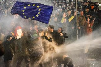 Protesters opposing the “foreign agent” bill brandish an E.U. flag as riot police spray them with a water canon outside of the parliament building in Tbilisi. March 7, 2023.