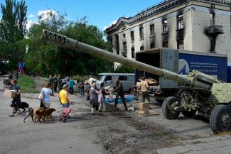 Жители Лисичанска получают гуманитарную помощь рядом с выставкой трофейных украинских танков и другого вооружения. Сейчас город находится под контролем ЛНР.