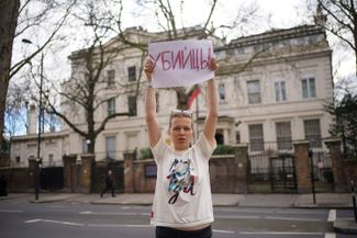A protester outside of the Russian Embassy in London. The sign reads: “Murderers.”
