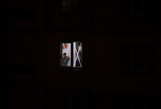 Жительница Киева снимает полоски скотча с окна: его горожане используют для защиты от осколков стекла во время обстрела. В ее квартире включено автономное освещение, в городе нет электричества. Ноябрь 2022 года 
