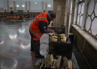 Работник вокзала делает чай для пассажиров. Он использует дровяную печь, установленную для обогрева. 25 ноября 2022 года