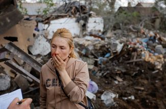 Жительница Донецка разговаривает со следователем, который собирает данные о ракетной атаке, на фоне своего разрушенного ударом дома