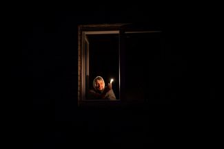 Пожилая жительница Бородянки со свечой в окне своего дома