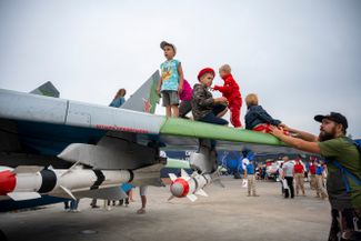 Children playing on the wing of a fighter jet. A mockup of an air-to-air missile can be seen underneath the wing. 