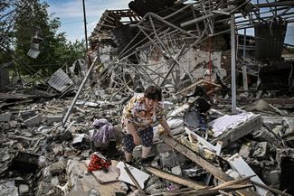 Местная жительница ищет свои вещи в развалинах дома, разрушенного в результате обстрела