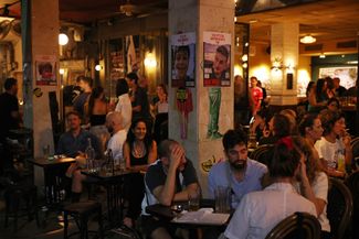 Посетители одного из баров в Тель-Авиве. Рядом с ними на стенах — плакаты с фотографиями заложников. На каждом надпись «Верните его домой немедленно». 2 ноября 2023 года