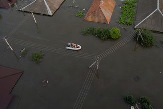 Жители Херсона на резиновой лодке — на одной из затопленных улиц города. 7 июня 2023 года