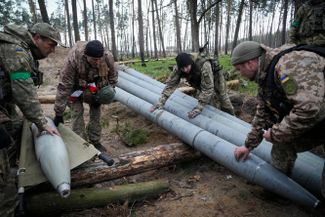 Украинские военные осматривают боеприпасы для систем залпового огня, которые остались в селе Березовка Киевской области после отступления российских войск
