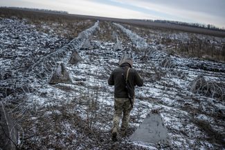 Украинский военный идет вдоль «зубов дракона» и колючей проволоки рядом с линией фронта в Харьковской области (где именно — не уточняется)