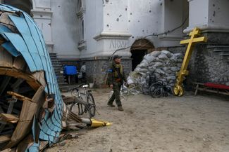 Украинский военный во дворе одного из храмов, который подвергался обстрелам. Видны защитные мешки с песком и надпись: «Люди», которая сигнализирует, что тут укрываются мирные жители