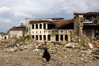 Женщина и ее собака рядом с руинами, которые так и не разобрали за год. Область Хатай, Турция