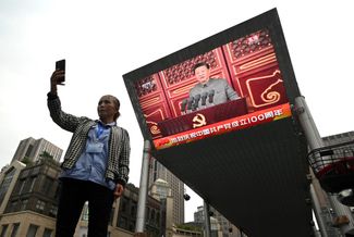 Женщина делает селфи на фоне экрана в Пекине, на который транслируется речь председателя КНР Си Цзиньпиня на площади Тяньаньмэнь. 1 июля 2021 года