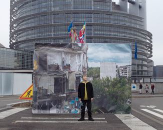 11-летний Александр на фоне фотографии разрушенных домов в Изюме Харьковской области, сделанной Евгением Малолеткой. Кадр можно было увидеть рядом со зданием Европейского парламента в Страсбурге
