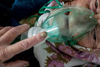 Пожилая женщина, госпитализированная с COVID-19, дышит с помощью кислородной маски. Город Почаев, Украина, 1 мая 2020 года