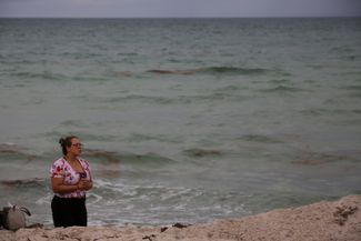Женщина молится за погибших и пропавших без вести на пляже Серфсайд.