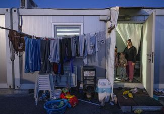 Женщина стоит со своими детьми в дверях временного «контейнерного» дома. Снимок сделан недалеко от города Кахраманмараш в Турции
