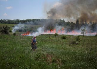Местная жительница смотрит на траву, загоревшуюся во время артиллерийской перестрелки между украинскими военными с одной стороны и силами России и самопровозглашенных ДНР и ЛНР — с другой