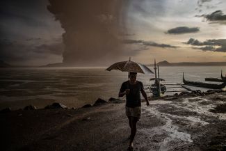 Местный житель прогуливается вдоль озера во время извержения вулкана Тааль на Филиппинах. Власти начали эвакуацию людей, когда вулкан начал извергать пепел высотой до километра. 12 января 2020 года