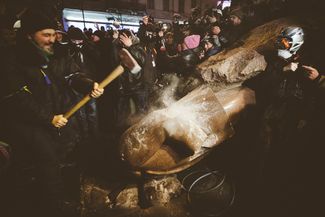 Демонстрант пытается расколоть памятник Ленину, который был сброшен с постамента участниками протестов в Киеве. 8 декабря 2013 года.