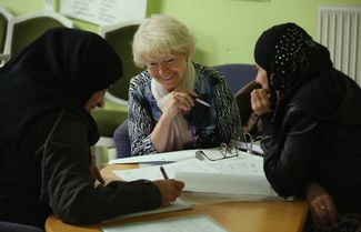 A volunteer teaching German to female refugees from Syria (on the left) and Chechnya (on the right) in a refugee center. Berlin, November 10, 2015