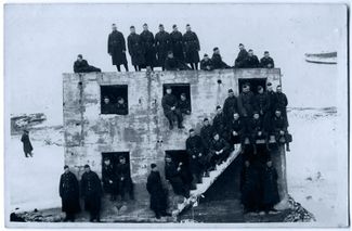 Latvian army soldiers pose with the same Battery No. 3 structure in the 1920s or 1930s. The photo shows a considerable distance between the building and the water’s edge. 