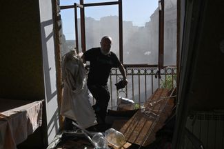 Жители дома, частично разрушенного российским ударом, выносят из квартир уцелевшие вещи