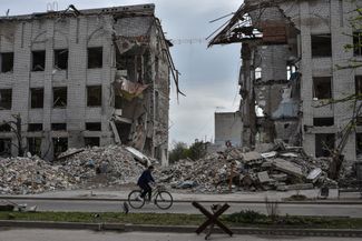 Местная жительница на фоне здания, разрушенного в результате российского обстрела