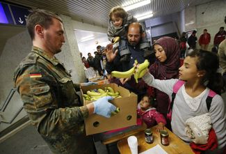 Немецкий военнослужащий раздает еду беженцам на станции Шенефельд в Берлине