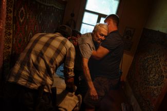 Члены гуманитарной организации Refugease поднимают из постели 84-летнего жителя Краматорска