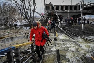 Civilians cross a river on a blown-up bridge in northern Kyiv