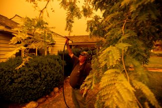 Житель Гринвилла Джерри Уиппл обрызгивает водой крышу своего дома, пока пожар «Дикси» подходит к городу, 23 июля 2021 года