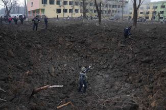 Украинские военные и спасатели рядом с воронкой от снаряда, упавшего во дворе мариупольского роддома. 9 марта 2022 года
