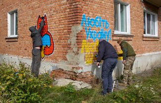 Уличные художники рисуют граффити в цветах флага Украины на стене одного из домов в Купянске
