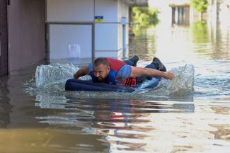 Житель Херсона плывет по затопленной улице на надувном матрасе