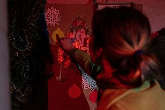 Жительница Бахмута развешивает на стене новогодние украшения. На листе бумаги в форме елочного шара написано «Желаю мира и любви»