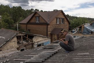 Местный житель Дмитрий сидит на крыше своего поврежденного дома