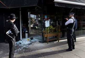 Прохожий и полицейские стоят у кошерного ресторана, в котором выбита витрина. Ресторан находится рядом с лондонским мостом, на котором появилась надпись «Free Palestine». 9 октября 2023 года